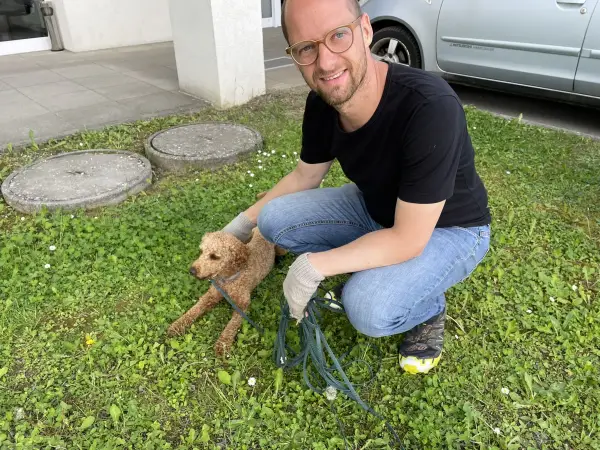Ich knie auf einer Wiese und lache in die Kamera, Rexi an der Leine
